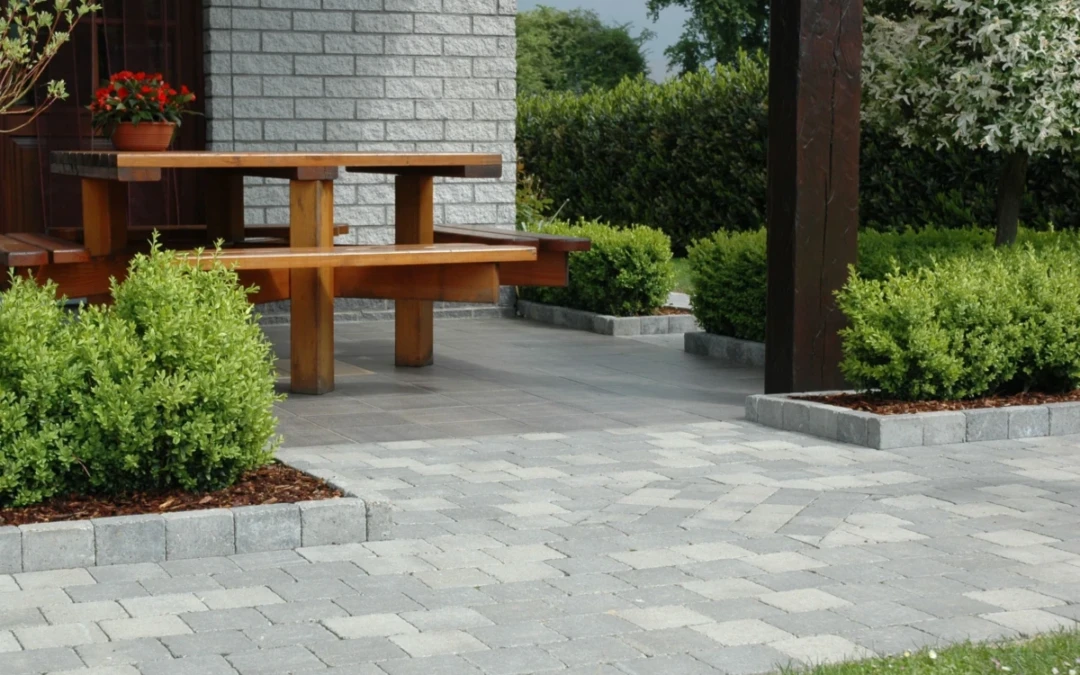 Terrasse abritée longée par une allée en pavés béton et bordée de plantations