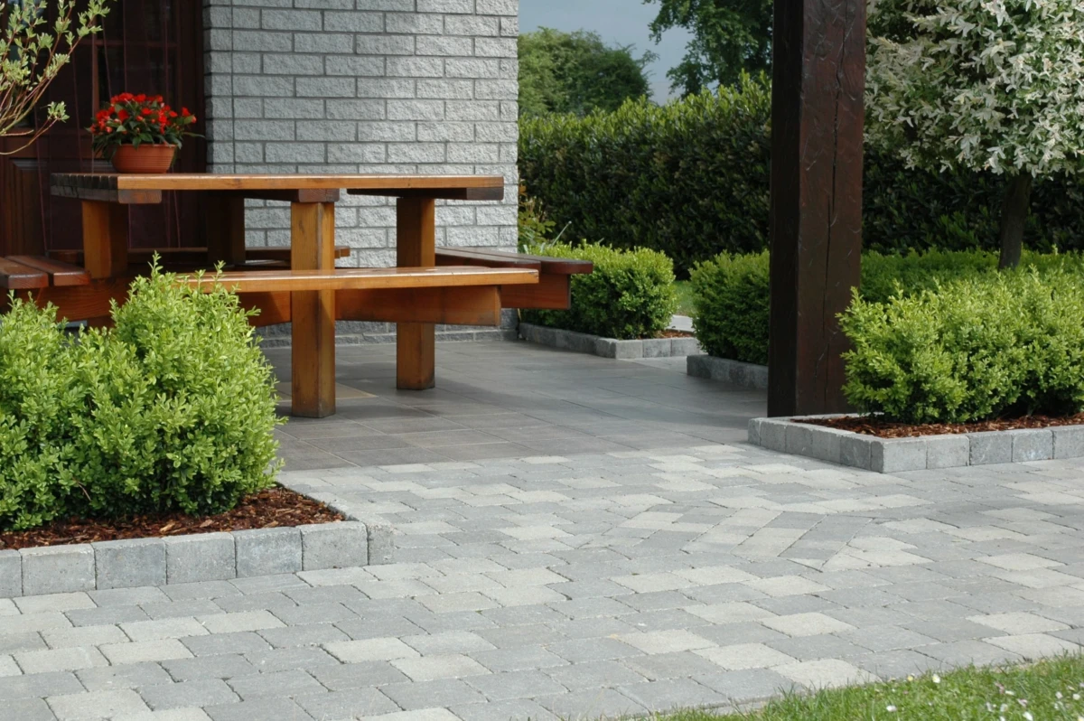 Terrasse abritée longée par une allée en pavés béton et bordée de plantations