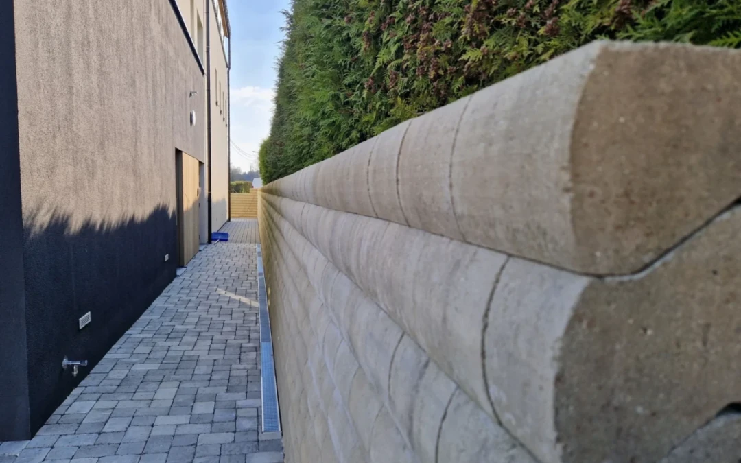 Mur de soutènement en Murasec coloris Cendre pour retenir la terre. Le mur borde une allée de pavé béton avec différentes nuances de gris.