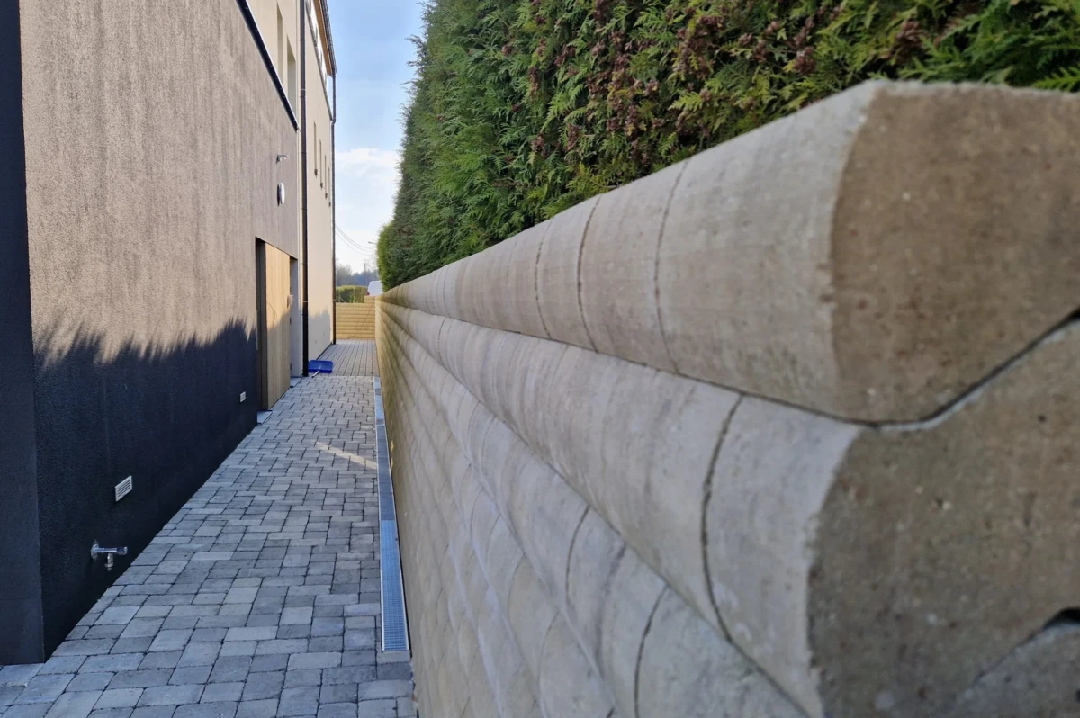 Mur de soutènement en Murasec coloris Cendre pour retenir la terre. Le mur borde une allée de pavé béton avec différentes nuances de gris.