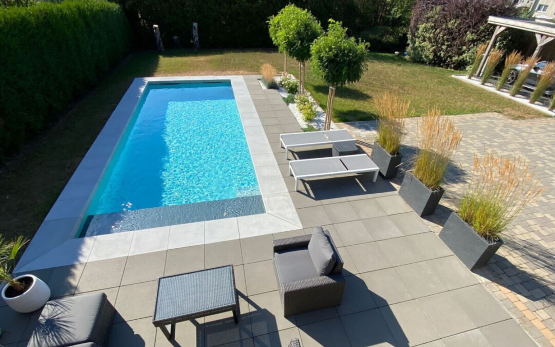 Margelles en béton coloris gris clair autour d'une piscine moderne bordée d'une terrasse.