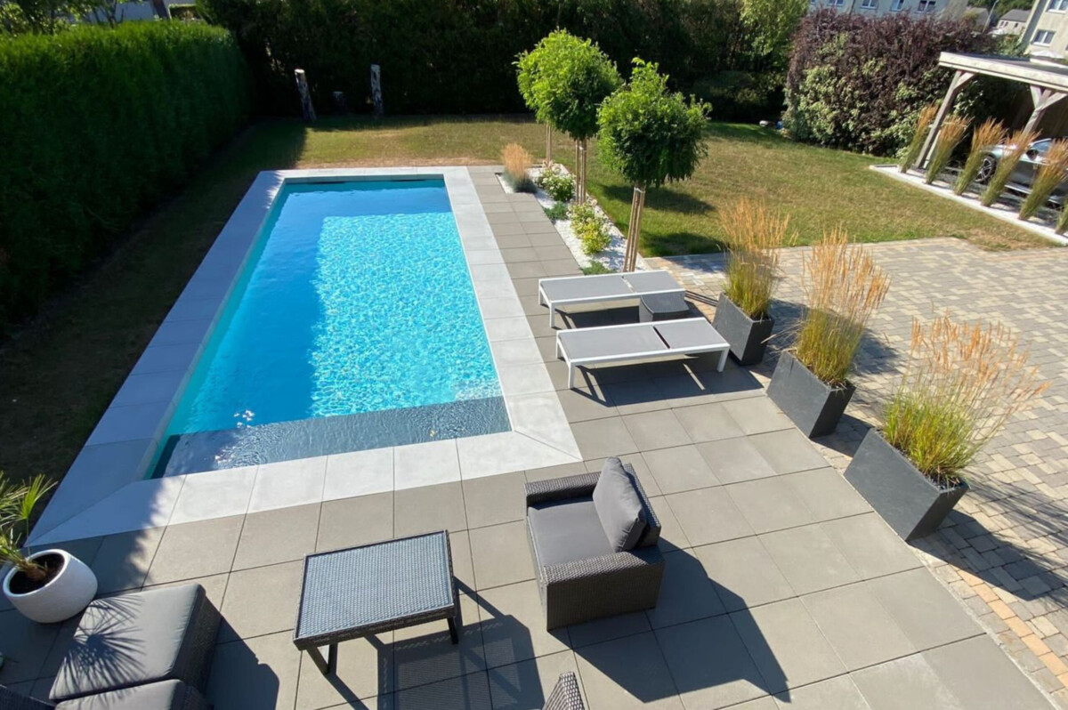 Margelles en béton coloris gris clair autour d'une piscine moderne bordée d'une terrasse.