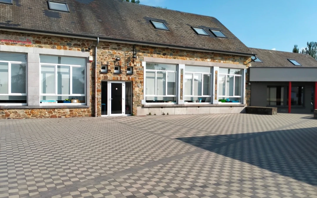 Pavés gris contrastés disposés en damier dans une cour d'école. Un cheminement traverse la cour depuis la porte d'entrée.